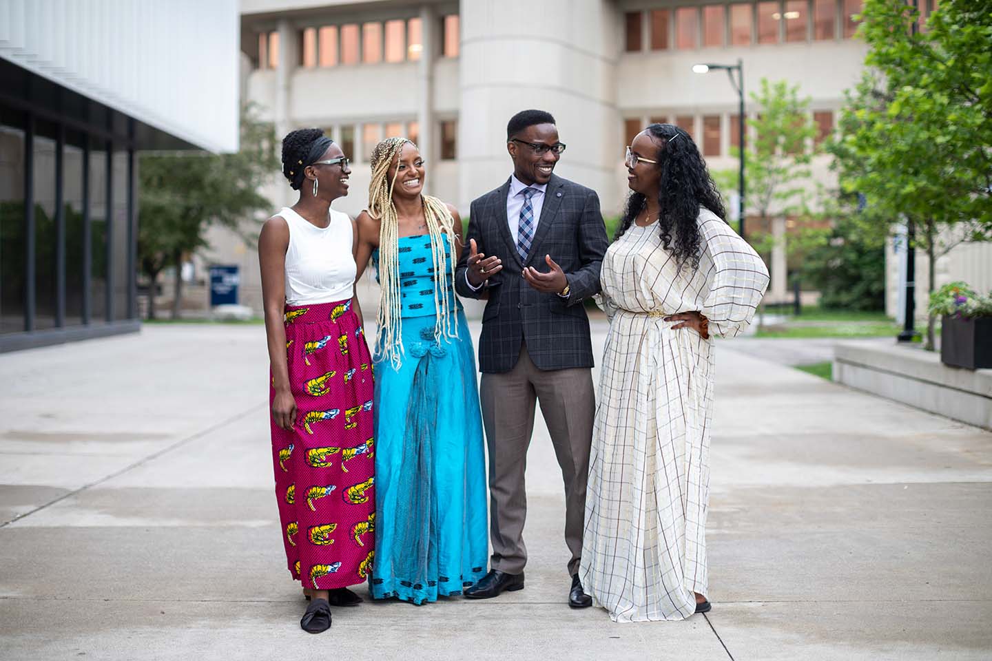 Four students smiling at each other in front of a university building