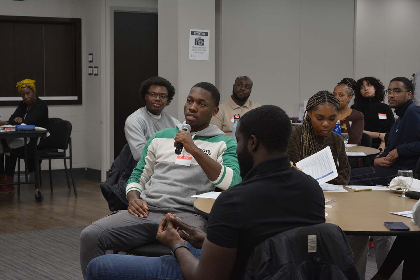 A student, sitting down, with a mic in their hand amidst a group of sitting down students