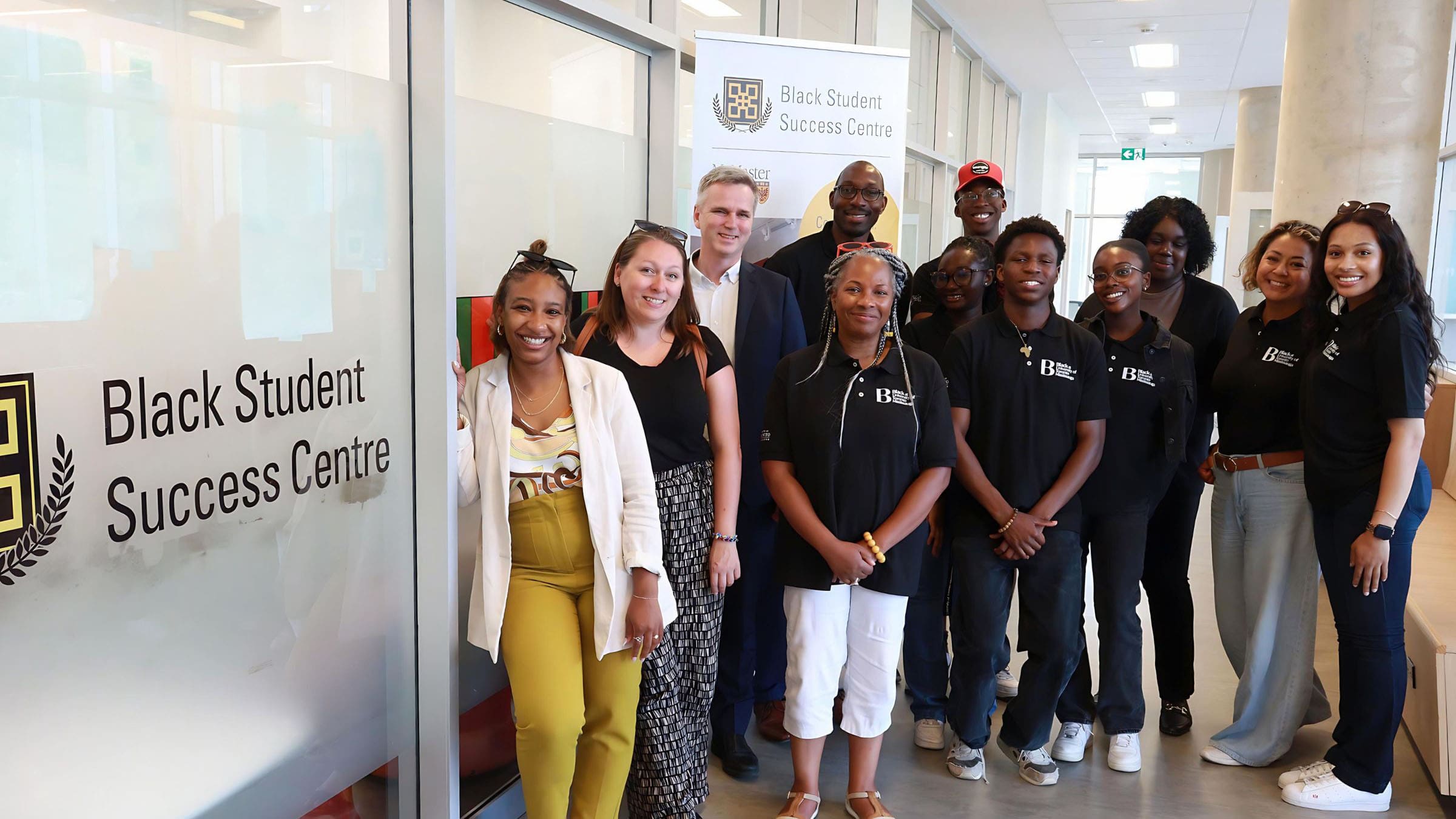 Group of people smiling wearing black at utm shirts in front of the Black Student Success Centre