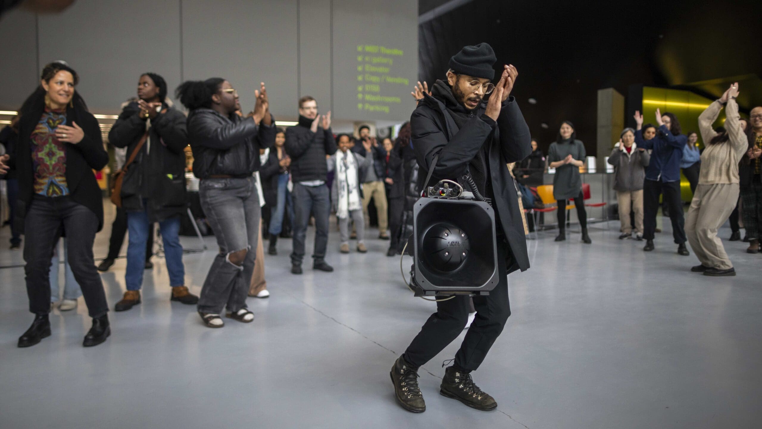 A man holding an LRAD and dancing with a large group of people